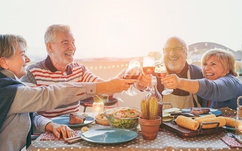Group of fun elderly folks clinking glasses over dinner outdoors 